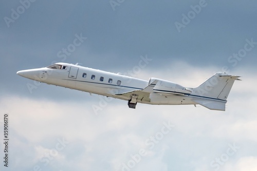 Side view of business jet airplane after taking off on grey white clouds in blue sky background. Fast modern aircraft for air transportation. Aviation technology. Travel and business concept.