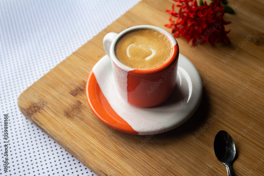 Freshly brewed sparkling coffee in a small orange and white mug. Cup with typical Brazilian drink on a wooden board. Copy space.