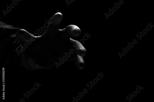Foto Close up scary hand of mysterious criminal in black glove reaching from the dark