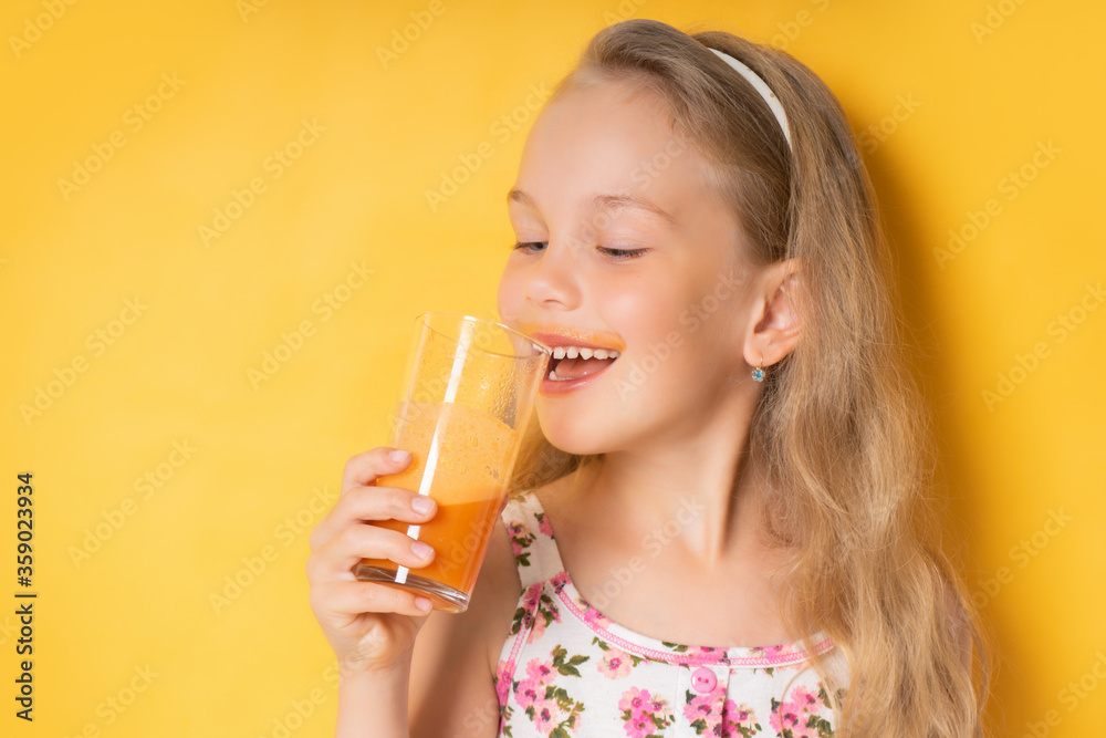 Nice little girl with waving blond hair enjoying carrot juice with great pleasure showing beautiful smile. Close up shot isolated on yellow, copy space. Childhood, healthy food, vitamins, summer time Nice little girl with waving blond hair enjoying carrot juice with great pleasure showing beautiful smile. Close up shot isolated on yellow, copy space. Childhood, healthy food, vitamins, summer time