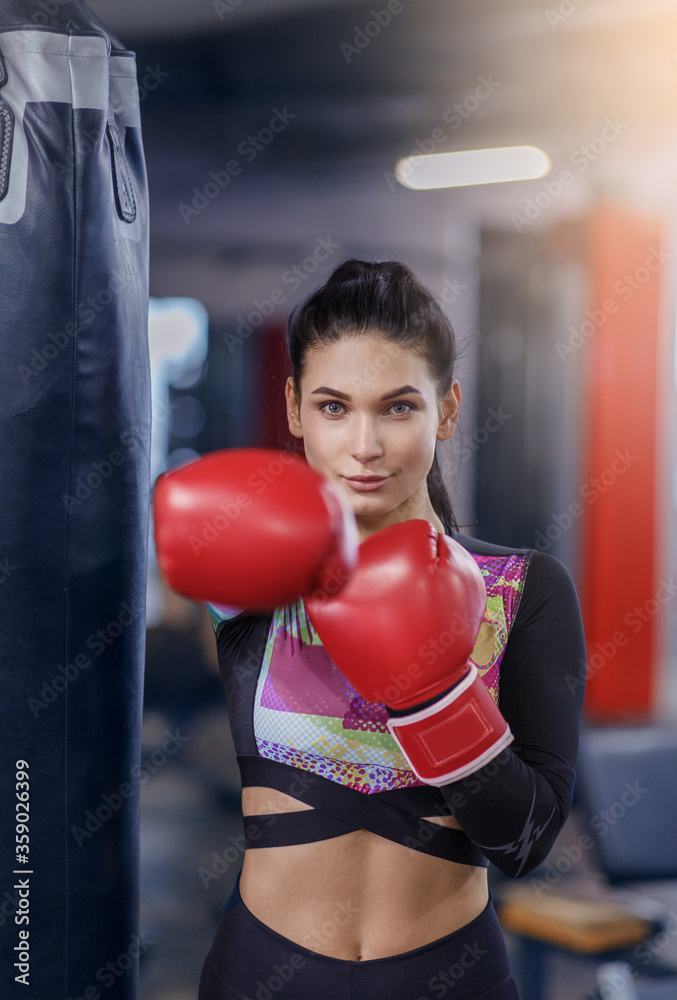 Millennial female boxer in gloves punching ball at sports club