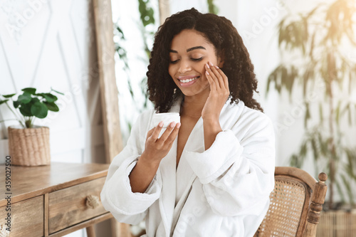 Skin Hydration. Beautiful young woman in bathrobe applying cream on her face