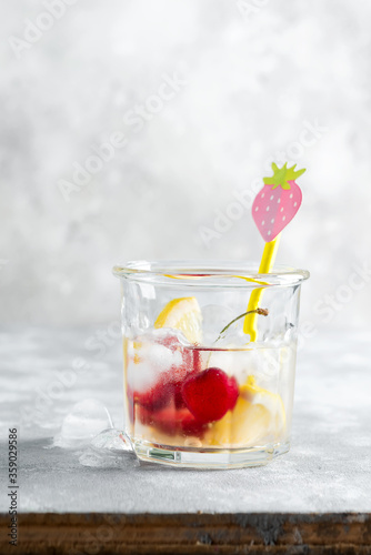 Refreshing homemade cold lemonade from berries and lemon in a glass with ice cubes on a marble grey table.