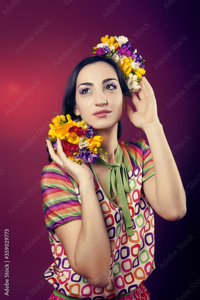 Naklejka premium Portrait of a cute girl with bright makeup and with the blooming freesias on his head and hands on a red background in the Studio.