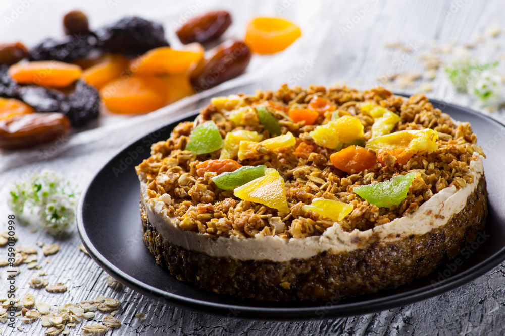 Diet cake with granola, dried fruits and candied fruits on a black plate on a white wooden table