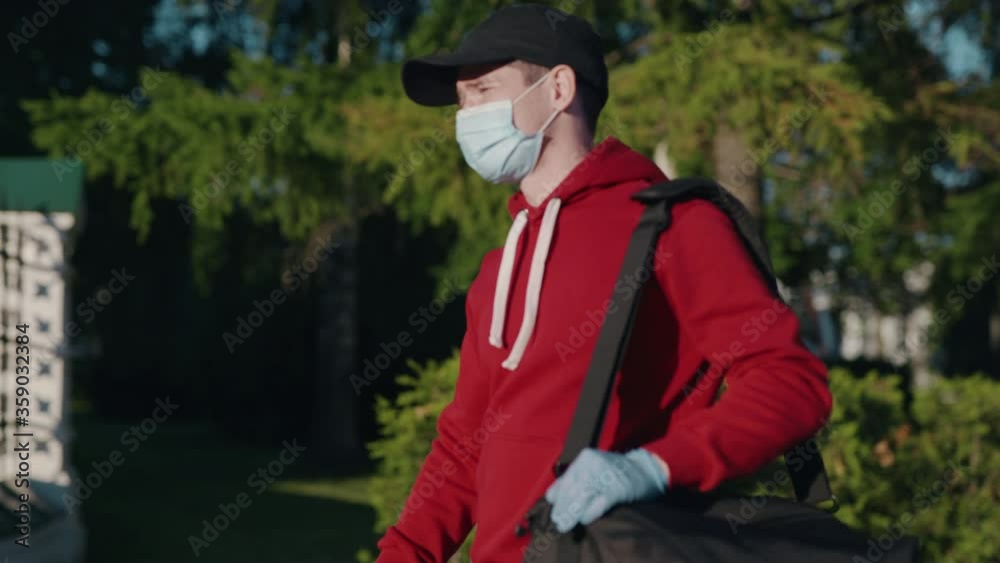 Online shopping and Express e-commerce. Delivery man in gloves and mask carrying bag looking in smartphone and walking at city street during pandemic time. Food supermarket home delivery. Online shopping and Express e-commerce. Delivery man in gloves and mask carrying bag looking in smartphone and walking at city street during pandemic time. Food supermarket home delivery.