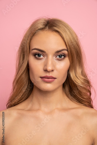 Beautiful sensual topless woman with long blonde hair posing isolated over pink background. Beauty concept