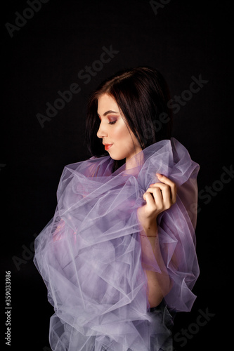 A beautiful, delicate girl with dark hair, wrapped in a tulle cloth.