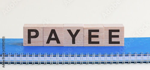 PAYEE - a word made of wooden blocks with black letters, a row of blocks is located on a blue Notepad. White background, front view. Promotion code, promo code concept.