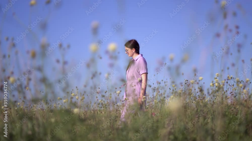Girl in purple dress walks through the field with field flowers Girl in purple dress walks through the field with field flowers