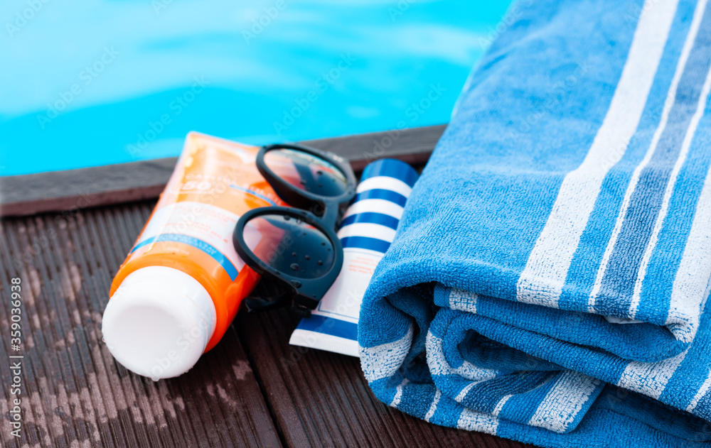 Φωτογραφία sun glasses, tube of sunscreen cream, blue towel near swimming pool, tropical background
