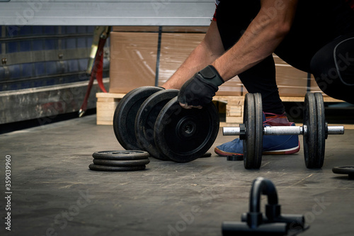 Man preparing the dumbbells for training in a warehouse.