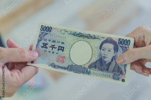 Close up of hand paying or giving cash money Japanese yen banknote to another to person. The yen is the official currency of Japan. Money, loan and corruption concepts
