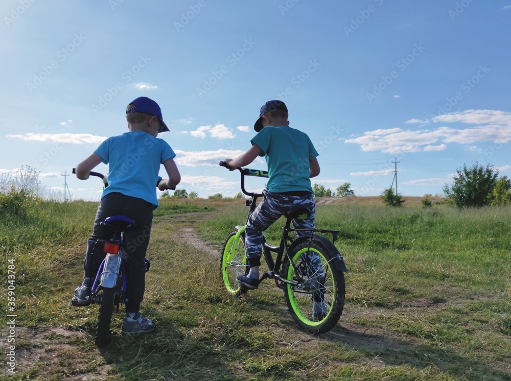 two boys play sports and ride bicycles in a field on a country road