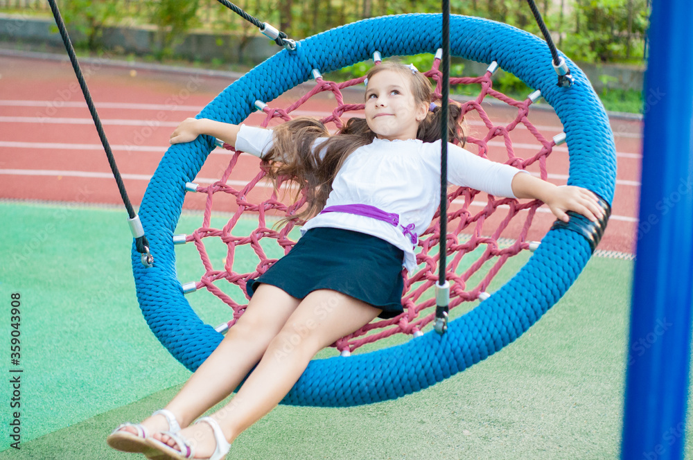 little smiling girl in school uniform on a swing outside little smiling girl in school uniform on a swing outside