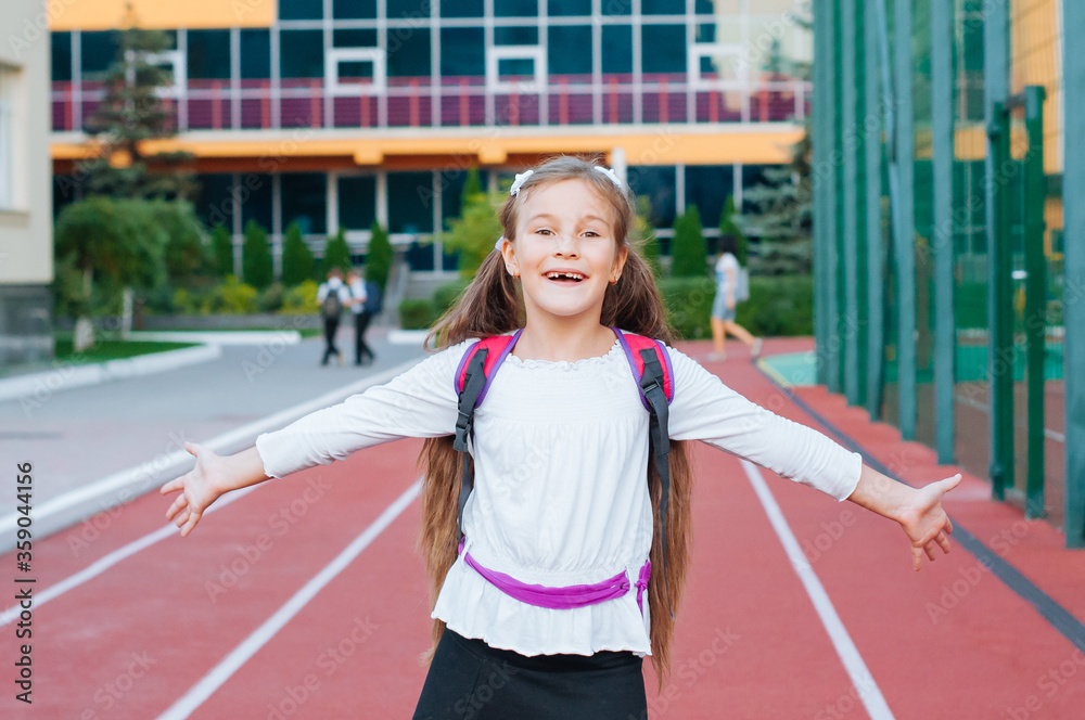 little smiling girl in school uniform with backpack outside