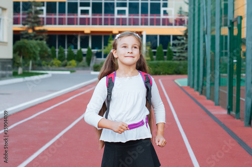 little smiling girl in school uniform with backpack outside