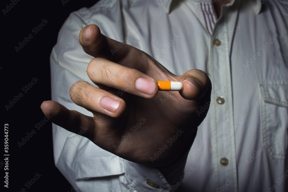 Fototapeta premium Male hand holds a pill. A man in a white shirt. Medicine for business.