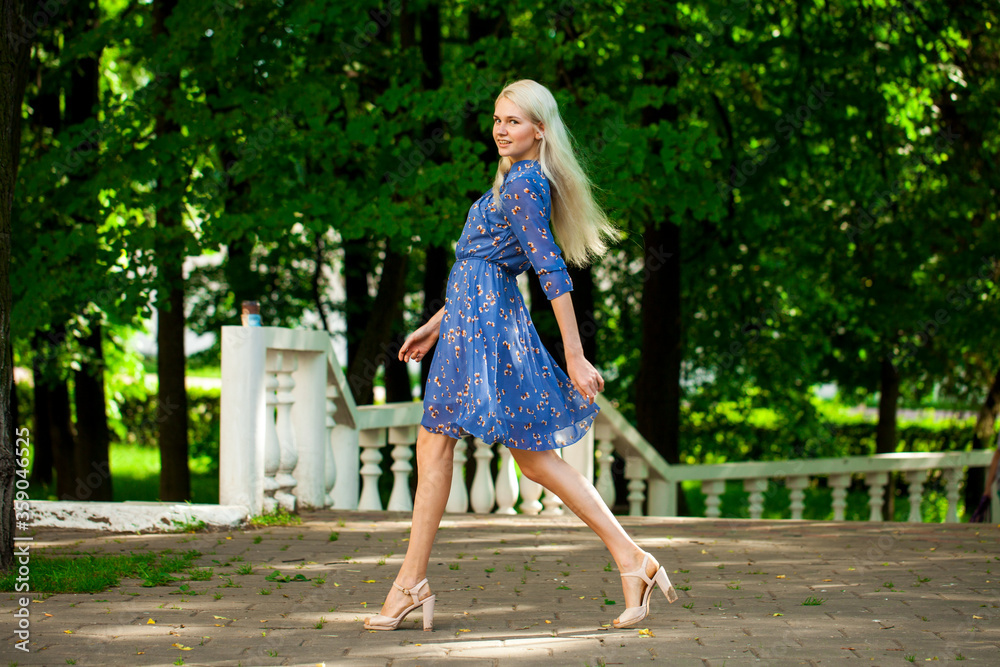 Portrait of a young blonde woman in blue dress walking in summer parkpark Portrait of a young blonde woman in blue dress walking in summer parkpark
