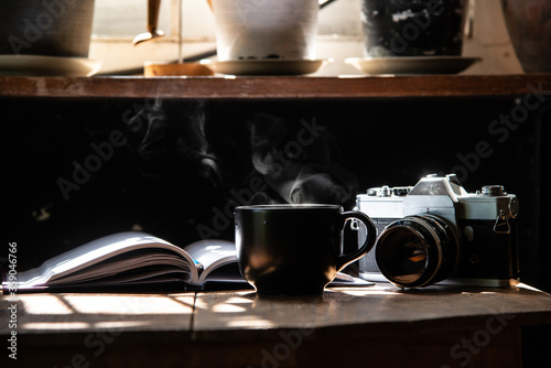 morning light refreshing black cup of hot coffee and stream with silver vintage camera and white page writing diary on wood table focus on camera stock photo