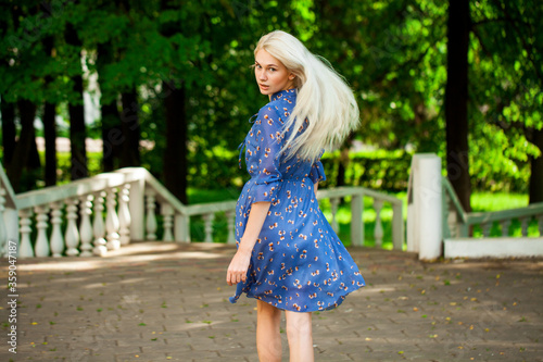 Portrait of a young blonde woman in blue dress walking in summer parkpark