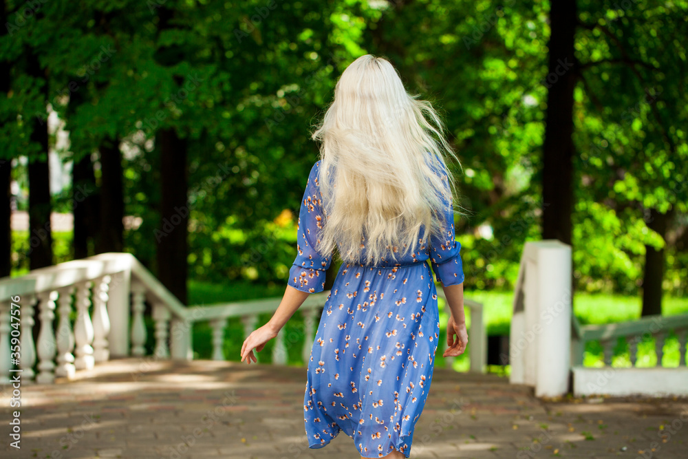 Portrait of a young blonde woman in blue dress walking in summer parkpark Portrait of a young blonde woman in blue dress walking in summer parkpark