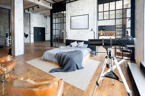 luxury studio apartment with a free layout in a loft style in dark colors. Stylish modern kitchen area with an island, cozy bedroom area with fireplace and personal gym photo