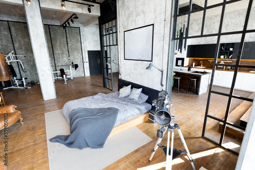 luxury studio apartment with a free layout in a loft style in dark colors. Stylish modern kitchen area with an island, cozy bedroom area with fireplace and personal gym