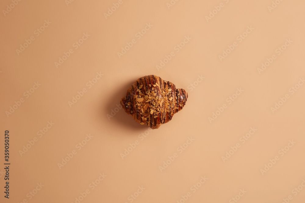 Whole delicious croissant sparkled with crumbs and chocolate, isolated on beige background. Junk food, calories, traditional french dessert. Tasty roll for breakfast. Confectionery and bakery concept Whole delicious croissant sparkled with crumbs and chocolate, isolated on beige background. Junk food, calories, traditional french dessert. Tasty roll for breakfast. Confectionery and bakery concept