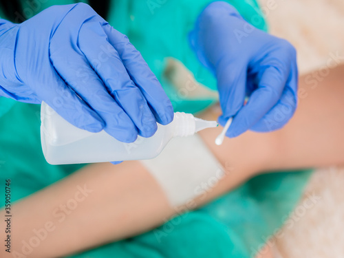 The doctor's hands in blue sterile gloves pours antiseptic on a cotton swab to treat the patient's abrasions.