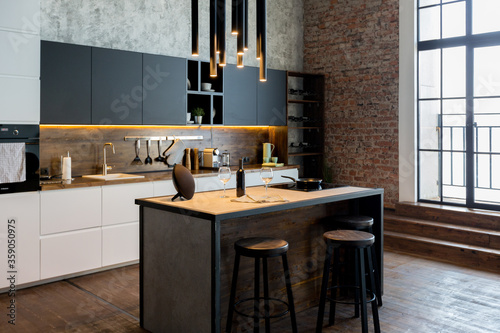 luxury studio apartment with a free layout in a loft style in dark colors. Stylish modern kitchen area with an island, cozy bedroom area with fireplace and personal gym