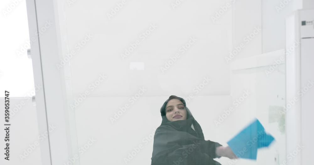 Muslim woman with headscarf celaning glass surface in modern house Muslim woman with headscarf celaning glass surface in modern house