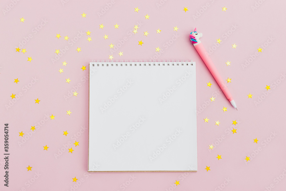 Empty notebook and unicorn pen on a pink background with golden star confetti. The concept of making wishes. Layout, top view, place for text Empty notebook and unicorn pen on a pink background with golden star confetti. The concept of making wishes. Layout, top view, place for text