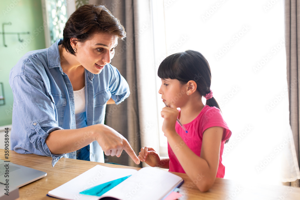 a mother explaining a lesson to her daughter who is working on her school homework a mother explaining a lesson to her daughter who is working on her school homework