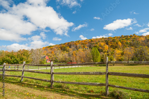 From American country road a rural landscape with red barn in distance beyond rustic post and rail fence in Kent county.