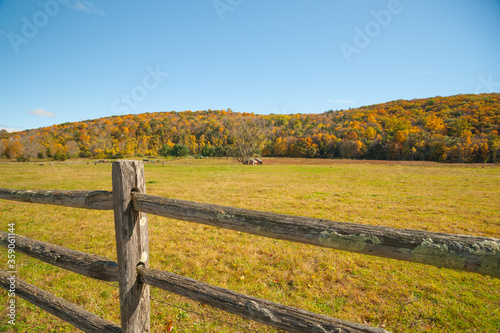 From American country road a rural landscape with farmhouse in distance beyond rustic post and rail fence in Kent county.