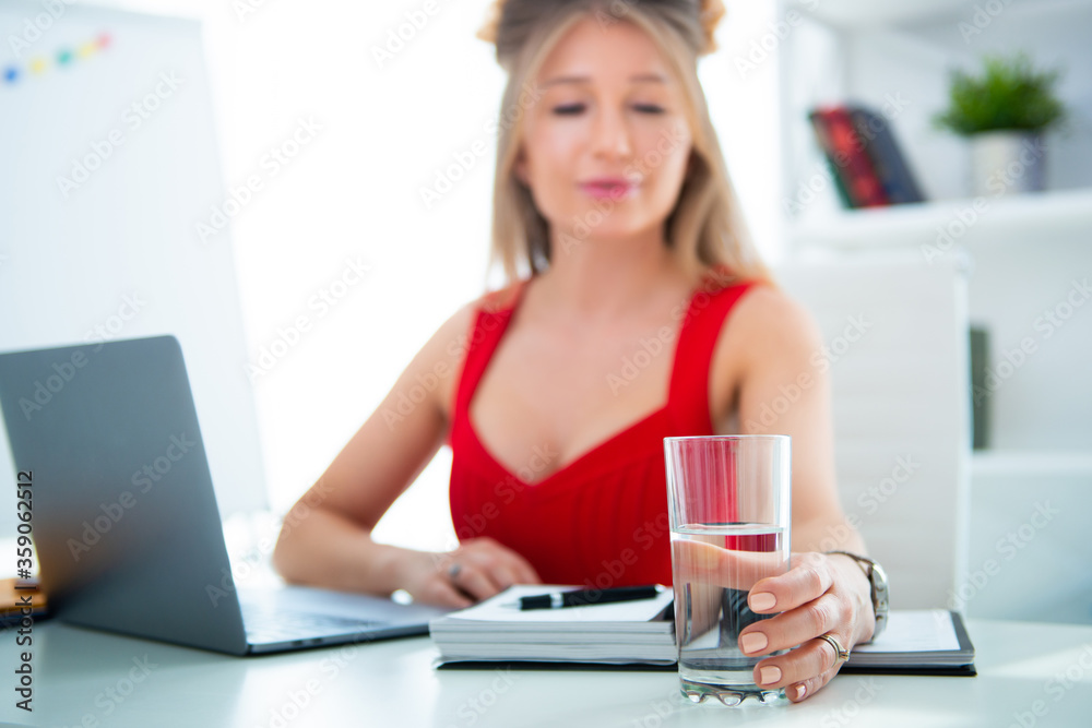 Young woman sitting in office at computer with a glass of clean water. Drinking plenty is the key to health, helps with stress and fatigue in business Young woman sitting in office at computer with a glass of clean water. Drinking plenty is the key to health, helps with stress and fatigue in business