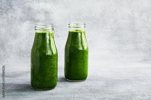 Green smoothie with spinach in small bottles on gray background. Copy space. Healthy food concept