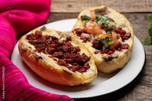 Mexican molletes with chorizo and fresh sauce on wooden background
