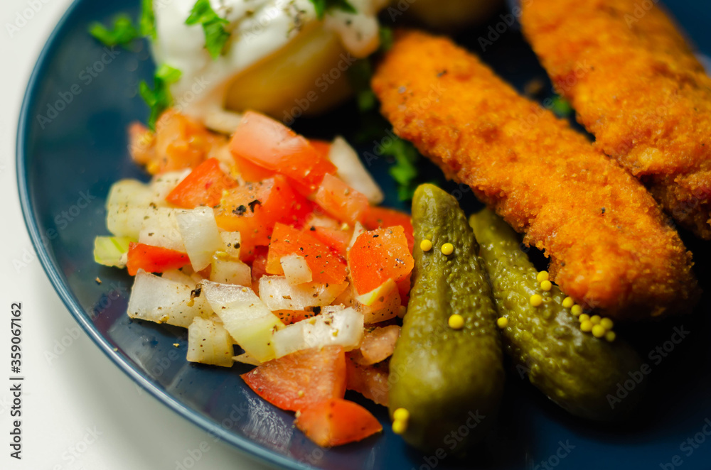 Breaded and herbed chicken breast fillet served with mashed potatoes, tomato salad with onions and gherkin Breaded and herbed chicken breast fillet served with mashed potatoes, tomato salad with onions and gherkin