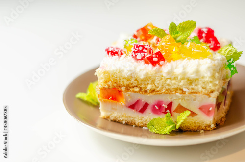 A portion of cream cake with pieces of colorful jelly and sprinkled with coconut flakes