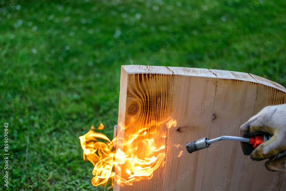 Fototapeta premium Bright flame when firing a wooden countertop with a gas burner, against the backdrop of a lawn with green grass (tree brushing).