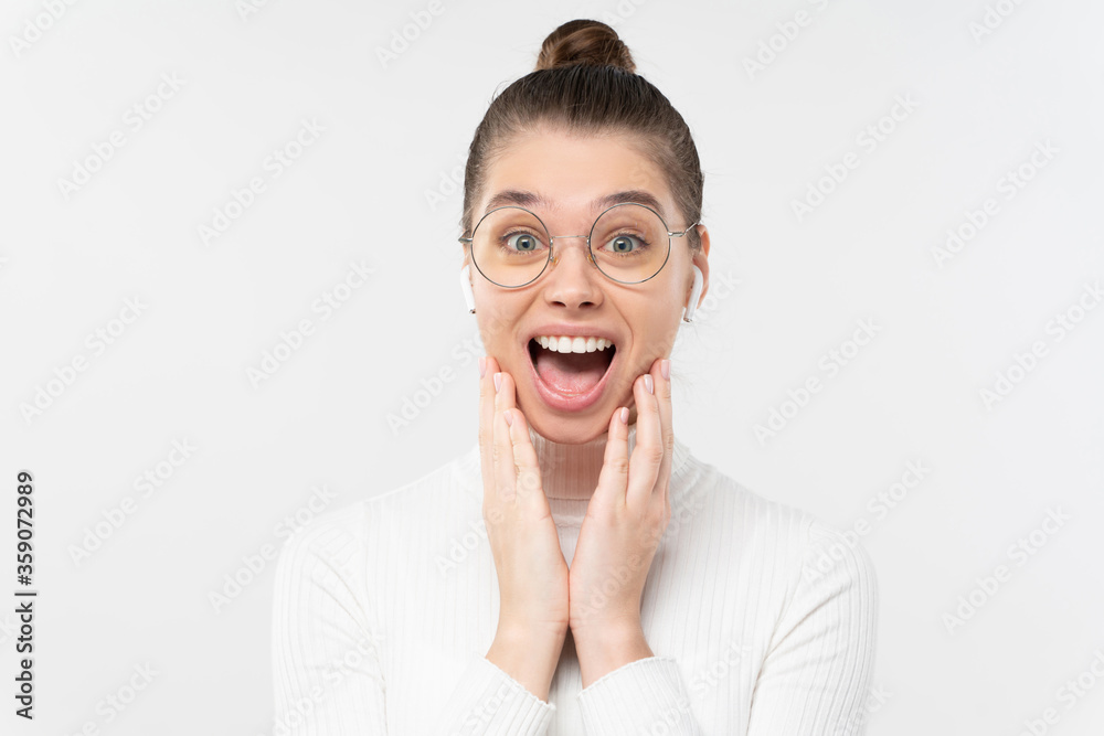 Young woman screaming with joy, feeling shocked by commercial offer, touching cheeks with palms, looking at camera with open mouth, isolated on gray background Young woman screaming with joy, feeling shocked by commercial offer, touching cheeks with palms, looking at camera with open mouth, isolated on gray background