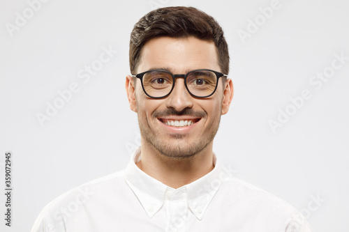 Close-up portrait of young handsome man wearing glasses and white shirt, isolated on gray background