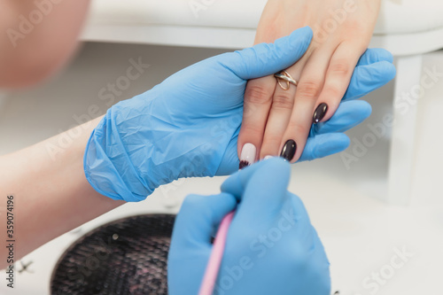 Manicure master in blue rubber gloves apply nail Polish client s nails. Hands close-up. Professional manicure beauty salon. Hygiene and hand care. Concept of beauty industry.