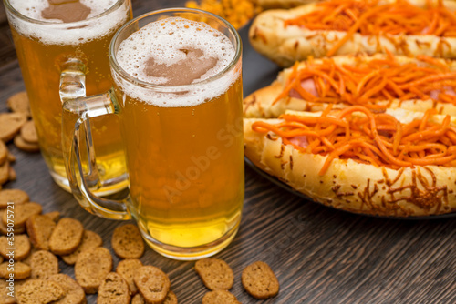 Photo of two glasses of beer with hot dogs, crackers, corn and peanuts. Beer snack and beer