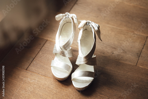 Pair of nice white wedding shoes against wooden floor background. Shoes are prepared for bride. Wedding day concept.