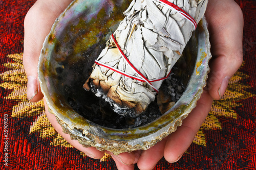 Photography A close up image of hands holding a abalone shell and white sage smudge stick