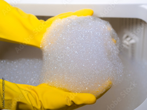 hands of a young girl with yellow gloves cleaning with foam from a washing machine