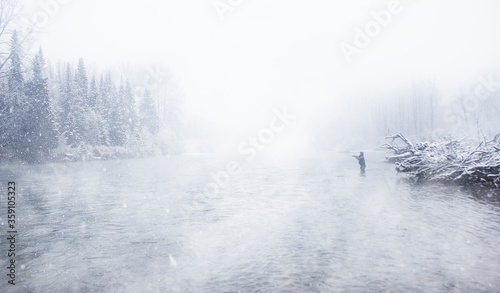 A sportfisherman with a fly rod winter river fishing in a snow storm on a foggy day in British Columbia Canada photo